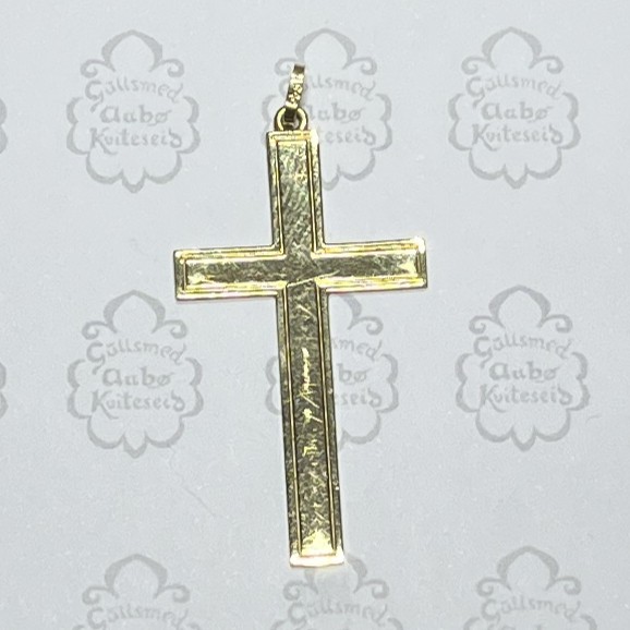 Gold cross pendant with a bail, hanging against a light patterned background.